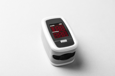 Photo of Modern fingertip pulse oximeter on white background, closeup