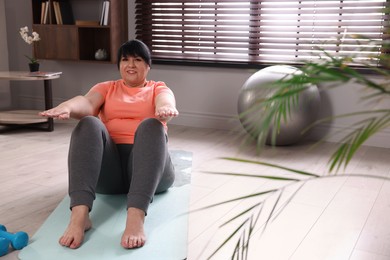 Overweight mature woman doing abs exercise on yoga mat at home, space for text