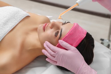 Young woman undergoing face rejuvenation procedure with darsonval in salon