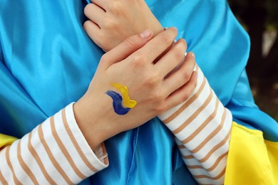 Woman with drawing of Ukrainian flag on hand against blurred background, closeup