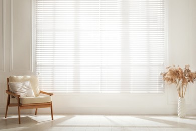 Cosy armchair and decor near large window with blinds in spacious room. Interior design
