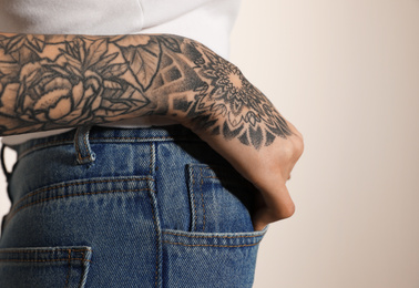 Woman with tattoos on arm against light background, closeup