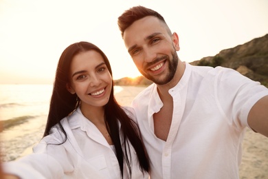 Happy young couple taking selfie on beach at sunset