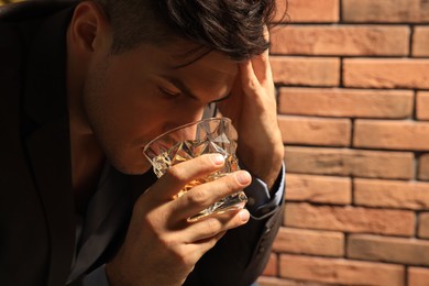 Addicted man drinking alcohol near red brick wall, closeup