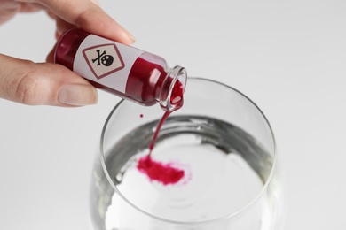 Woman pouring poison into glass of water on white background, closeup