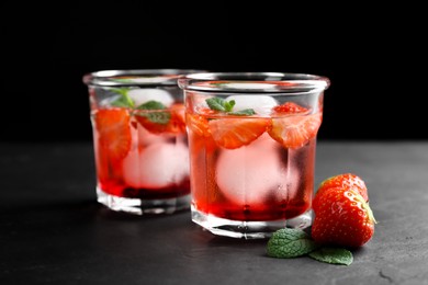 Delicious cocktails with strawberries, mint and ice balls on black table
