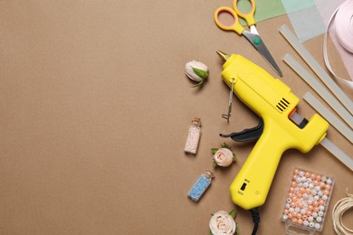 Hot glue gun and handicraft materials on brown background, flat lay. Space for text