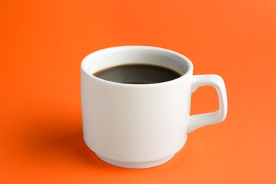 White mug of freshly brewed hot coffee on orange background