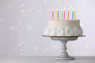 Birthday cake with burning candles on white table against blurred festive lights, space for text