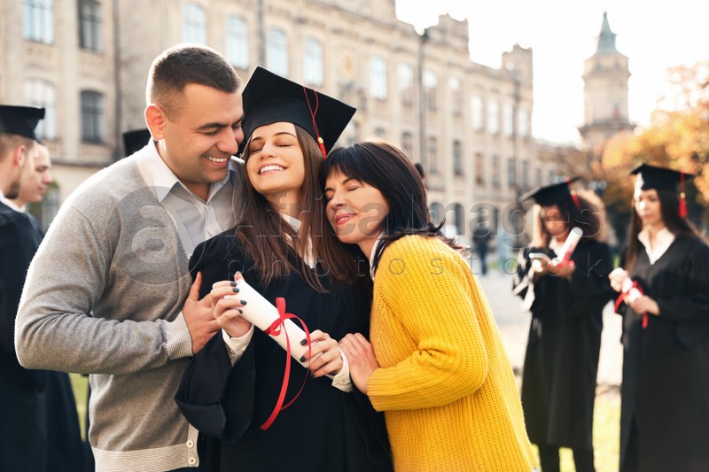 Happy student with parents after graduation ceremony outdoors