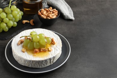 Brie cheese served with grape, cashew nuts and honey on dark grey table. Space for text