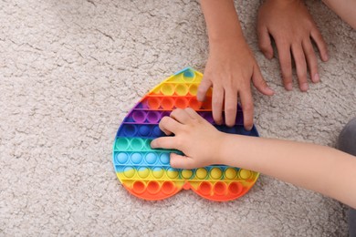 Little children playing with pop it fidget toy on floor, top view