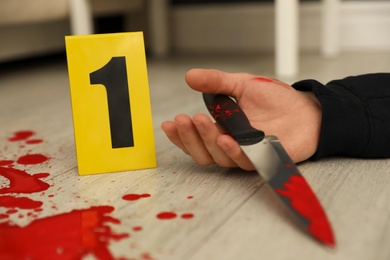 Crime scene marker and dead body with bloody knife on floor, closeup