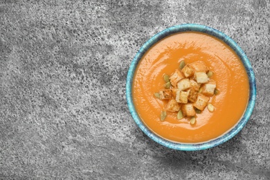 Tasty creamy pumpkin soup with croutons and seeds in bowl on grey table, top view. Space for text