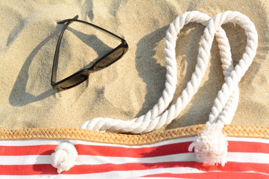 Stylish sunglasses and beach bag on sand, flat lay