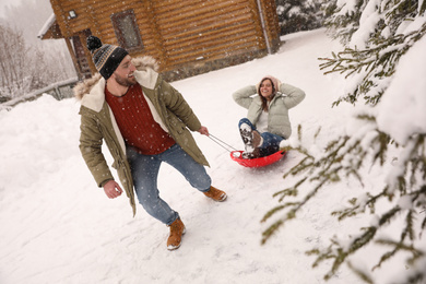 Young man pulling sled with his girlfriend outdoors on snowy day. Winter vacation