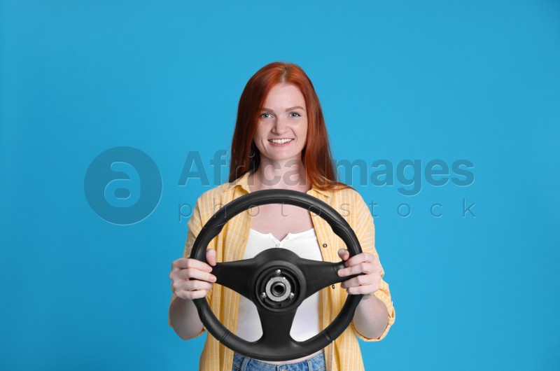 Happy young woman with steering wheel on light blue background
