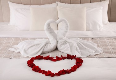Photo of Beautiful composition on bed. Swans made of towels and rose petals arranged in heart shape