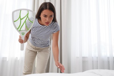 Photo of Young woman with electric fly swatter in bedroom. Insect killer