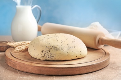 Raw dough with poppy seeds and rolling pin on wooden board