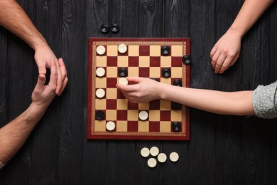 Photo of Man playing checkers with woman at black wooden table, top view