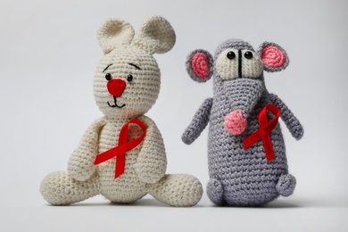Cute knitted toys with red ribbons on light grey background. AIDS disease awareness