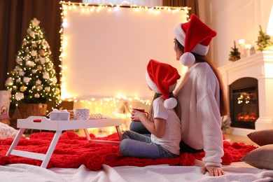 Mother and daughter watching movie using video projector at home. Cozy Christmas atmosphere