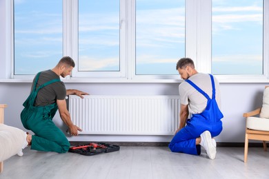 Professional plumbers installing new heating radiator in room
