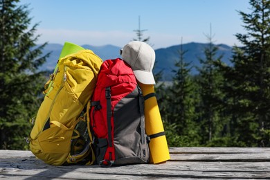 Photo of Backpacks, sleeping mats and cap on wooden surface outdoors, space for text. Mountain tourism