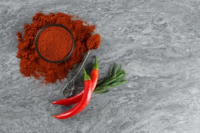 Ground red pepper with spoon and ingredients on grey marble table, flat lay. Space for text