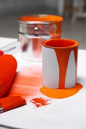 Photo of Cans of orange paint, brush and roller on white table indoors