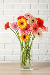 Photo of Bouquet of beautiful colorful gerbera flowers in vase on table against white brick wall