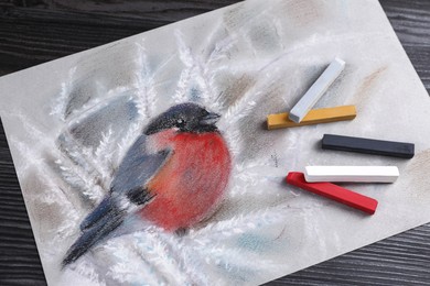 Colorful chalk pastels and beautiful painting of bullfinch on black wooden table, top view