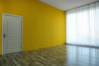 Empty room with yellow brick wall, large window and white door