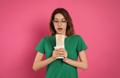 Photo of Emotional young woman with delicious shawarma on pink background
