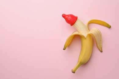 Banana with condom on pink background, top view and space for text. Safe sex concept