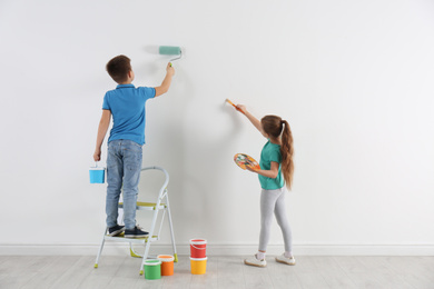 Little children painting on blank white wall indoors