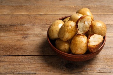 Photo of Bowl of tasty whole baked potatoes on wooden table, space for text