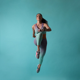 Athletic young woman running on turquoise background