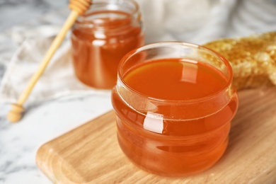 Glass jar with sweet honey on wooden board, closeup