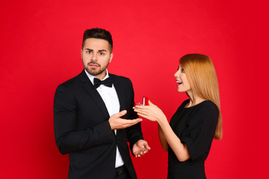 Young woman with engagement ring making marriage proposal to her boyfriend on red background