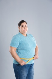 Photo of Overweight woman measuring waist before weight loss on color background