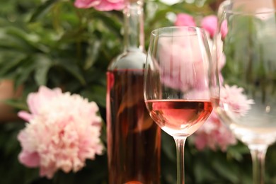 Glasses and bottle with rose wine against beautiful peonies, closeup. Space for text