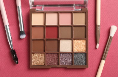 Photo of Eyeshadow palette with makeup brushes on pink background, flat lay