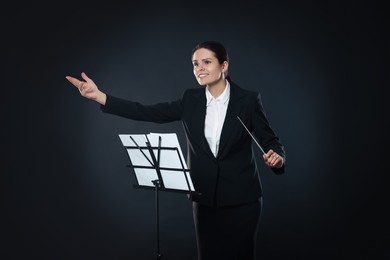 Happy young conductor with baton and note stand on dark background