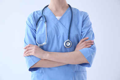 Young doctor with stethoscope on light background, closeup