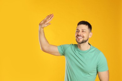 Photo of Cheerful man waving to say hello on yellow background