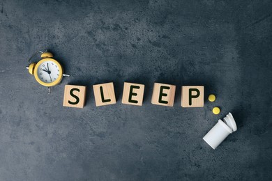 Word Sleep made of wooden cubes near pills and alarm clock on grey background, flat lay. Insomnia concept