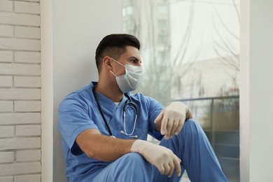 Sad doctor near window indoors. Stress of health care workers during coronavirus pandemic