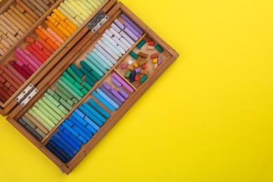 Set of soft pastels in wooden box on yellow background, top view with space for text. Drawing material